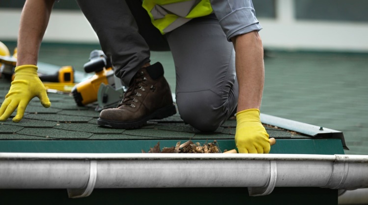 Working man removing pile of leaves from gutter